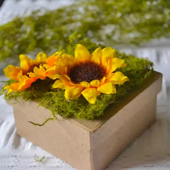 The Spotted Donkey artificial green moss mat topped with yellow sunflowers on a craft box for floral decor.