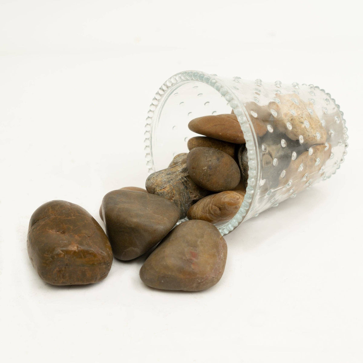 The Spotted Donkey multi-colored polished river rocks spilling from a clear glass vase on a white background.